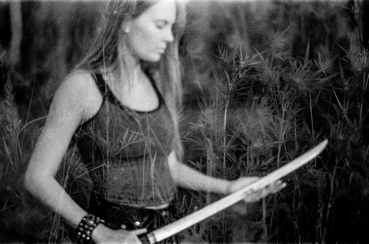 Black-and-white 35mm film portrait of a young woman holding a katana double exposed with the background