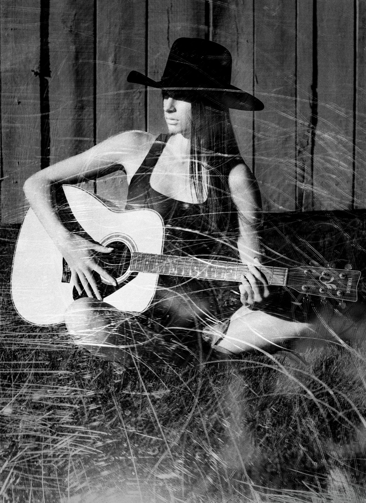 Abstract Black-and-white portrait of a young woman playing guitar behind scratched glass.