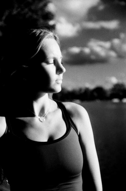 High-contrast near-infrared film Black-and-white portrait of a young woman wearing a tank top with dramatic side lighting, emphasizing the contours of her face and body