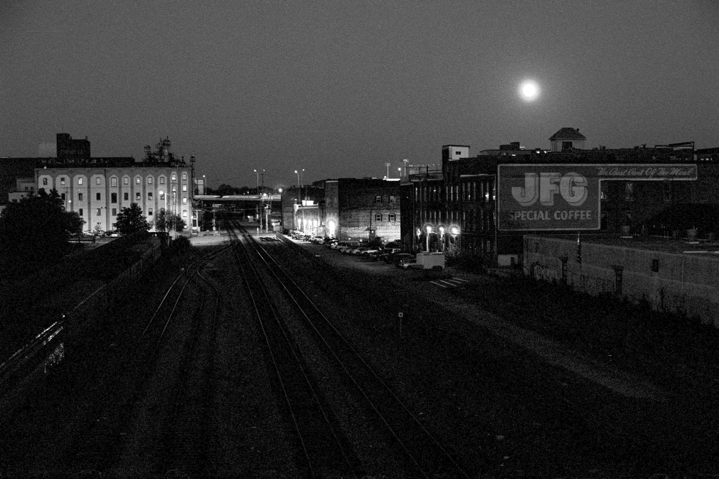 Train tracks at night with buildings and a moonlit sky.