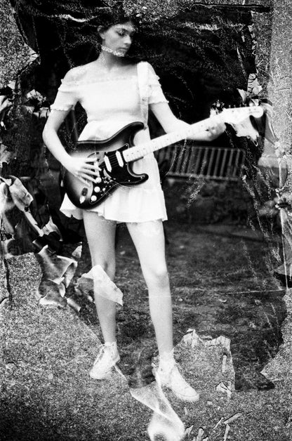 Abstract Black-and-white double exposure portrait of a young woman wearing a short white dress playing a Stratocaster electric guitar in the backyard