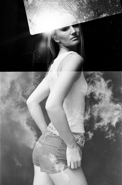 Abstract Black-and-white portrait of a young woman wearing shorts behind square glass and clouds