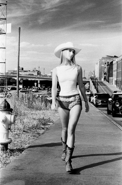 Black-and-white 35mm film portrait of a young woman walking in the old city side of Knoxville wearing a country style hat, shorts and boots